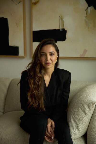 Editorial Headshot of a woman sitting on a couch with artwork on the wall in a black suit