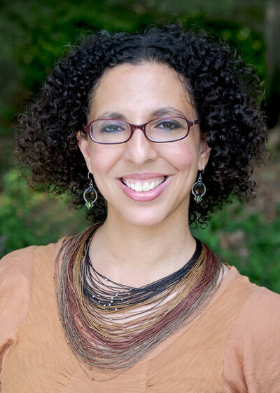 Black woman with short curly hair, wearing glasses, earrings, and a multi-layered necklace