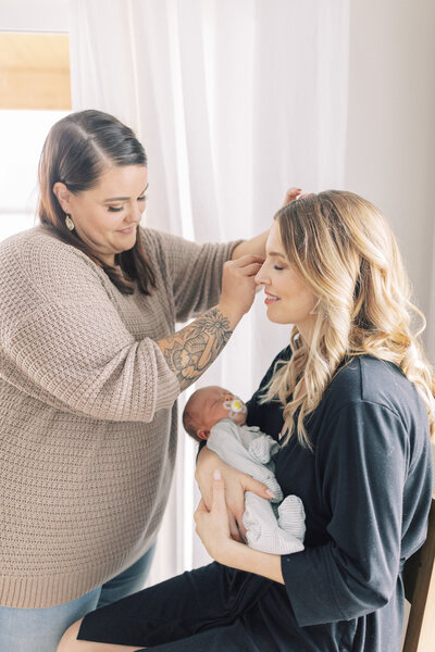 mother holding baby while having hair and makeup done for photoshoot with madison wi newborn photography, Talia Laird Photography