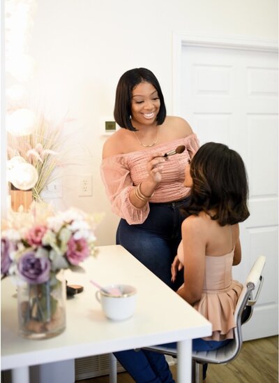 bridal make up artist whitney elise places powder on bride sitting in chair