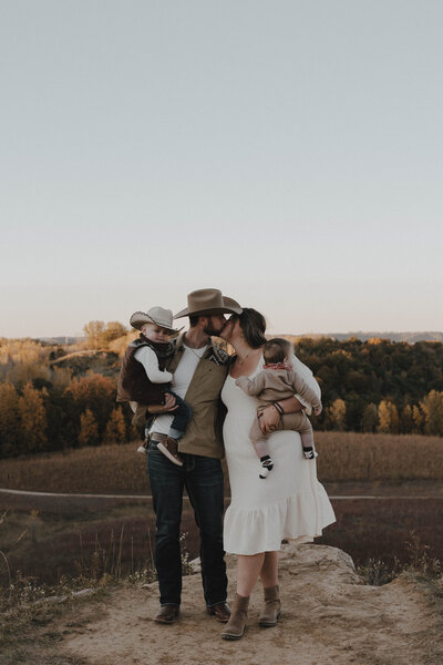 Parents with toddler and baby kissing on bluff in Wisconsin
