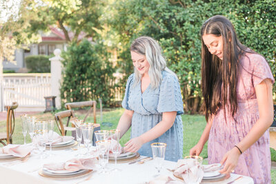 wedding vendors setting a table with plates, napkins, and glassware. Captured by a wedding day content creator