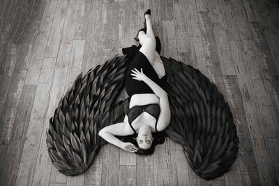 woman with large black wings prop posing in black and white boudoir portrait