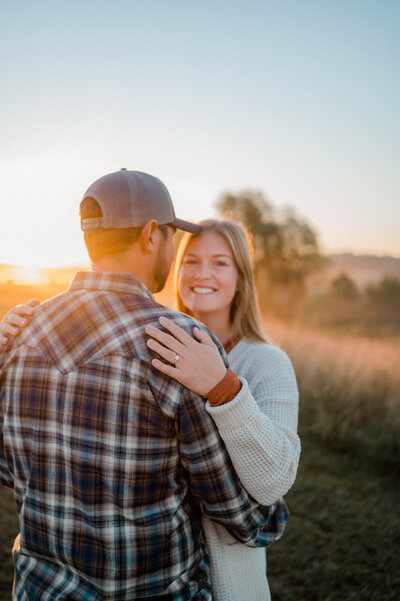 Couple poses for the camera at sunrise. Woman faces the camera smiling while man hugs her.