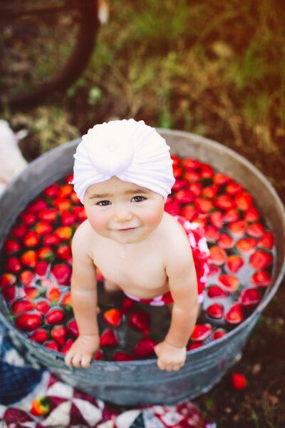Cute little girl sitting in a tub of strawberries