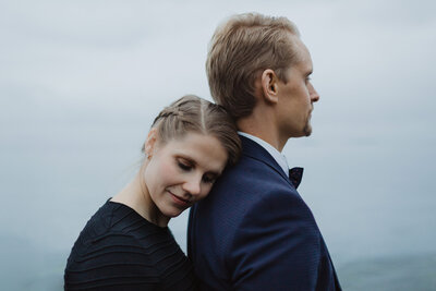 Bride in a black dress leaning her head against groom's upper back eyes closed in Helsinki in Finland.