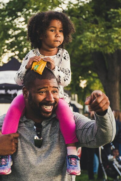 man with a little girl on his shoulders laughing and pointing