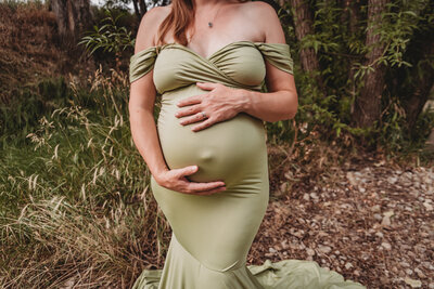 mom holding pregnant belly in green dress in Longmont Colorado