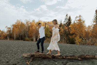 couple on black beach mn. man is helping women across a log on the beach