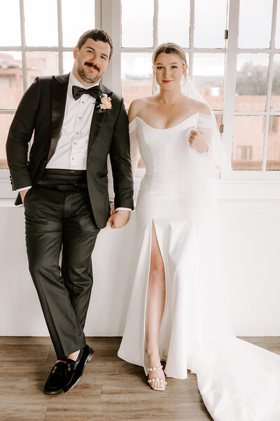 bride and groom holding hands leaning up against a wall
