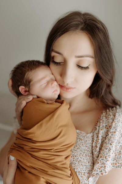 A woman holding her newborn baby in a brown wrap.