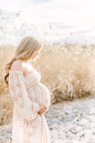 Pregnant mother to be wearing a white lace dress in a field of yellow grass