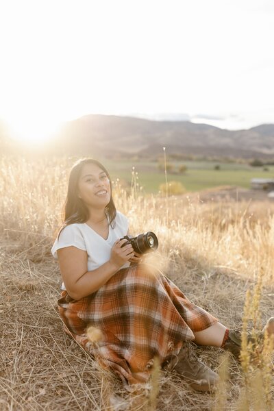 Meghan sits while holding a camera outdoors