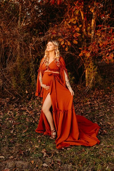 Maternity photography in Cleveland  TX- expectant mother in an elegant rust gown holding baby bump outdoors