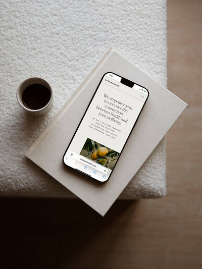 Mobile view of a custom Showit website design for a wellness brand, displayed on a smartphone atop a linen-bound book—clean, elevated UX created by Showit website designer A Design Haus.