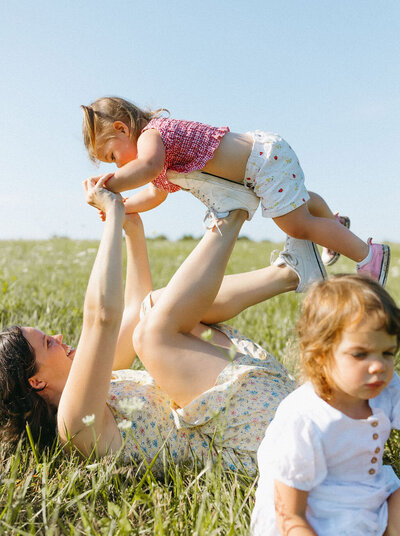 mom plays with toddlers in grassy field in blue skies