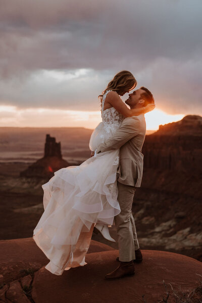bride and groom standing on a red rock formation with the desert in the background