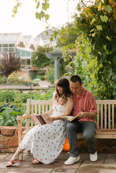 Couple sitting on a garden bench during their Colorado engagement session, reading together beneath a blooming tree at the Denver Botanic Gardens