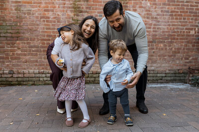 Family Photographer, a mom and dad playfully hold onto their children outside