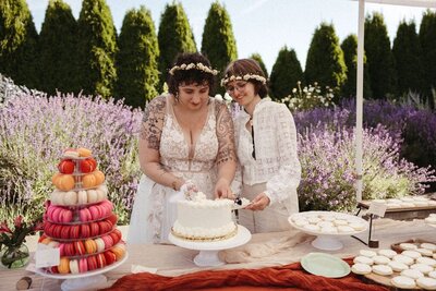 Newlywed brides cut their cake during a whimsical garden party wedding photographed by inclusive wedding photographer, Wilder Photographu