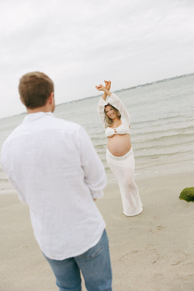 husband looking at his wife while shes posing with her arms up in front of the water