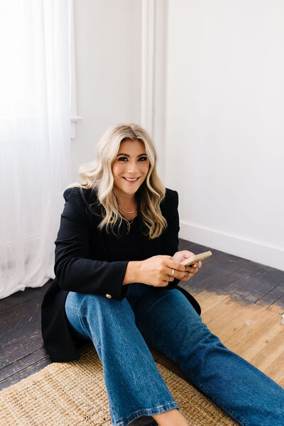 Calgary Realtor Leigh Kormos sitting on a brown rug in the corner of a house