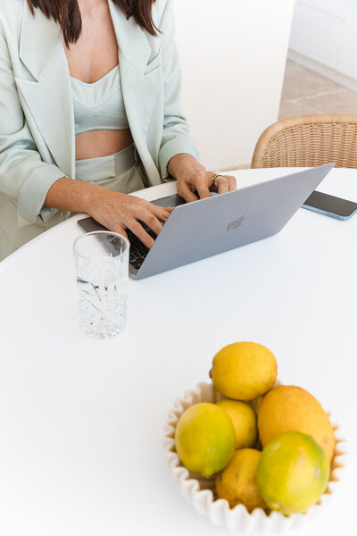 Lady sitting at a table with fruit and a Laptop open