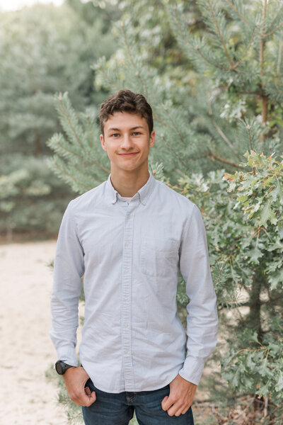 Senior boy smiling in front of pine tree at dunes.