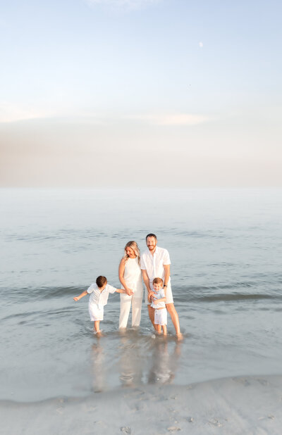 Family posing in the water at the beach while the sun sets