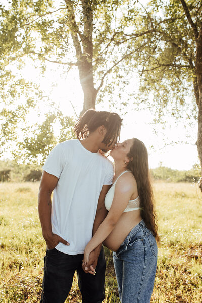 Expecting couple kisses in front of tree