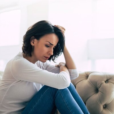 Woman Struggling With Hand on Head curled up on couch