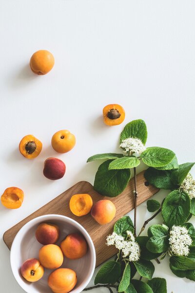Sliced peaches in a white bowl on a wooden cutting board next to a large plant