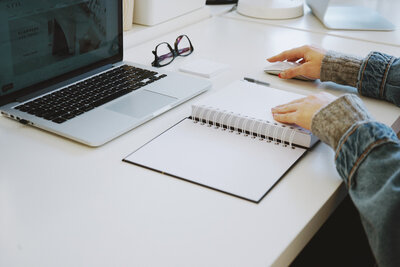 Hailey Ann Co Bookkeeper and Somatic Money Coach for Female Entrepreneurs sitting at computer with notebook, pen and computer mouse