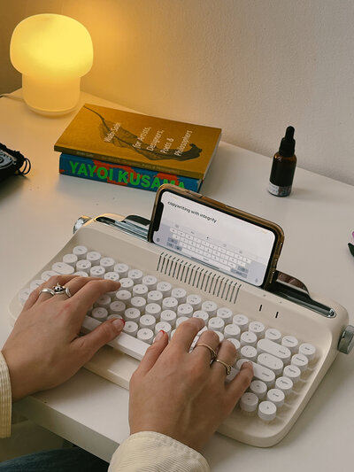 Hands typing on a vintage typewriter-looking keyboard attached her Margarita's phone, where you can see the words "copywriting with integrity" spelled out.