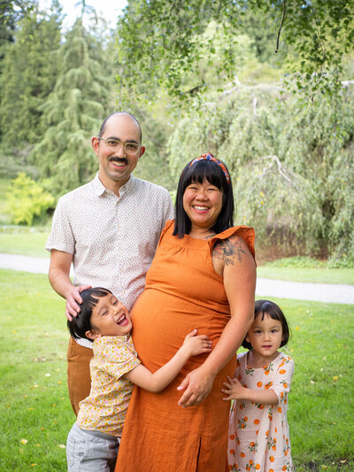 A family with a pregnant mother and two children laugh together as they play at University of Washington's arboretum