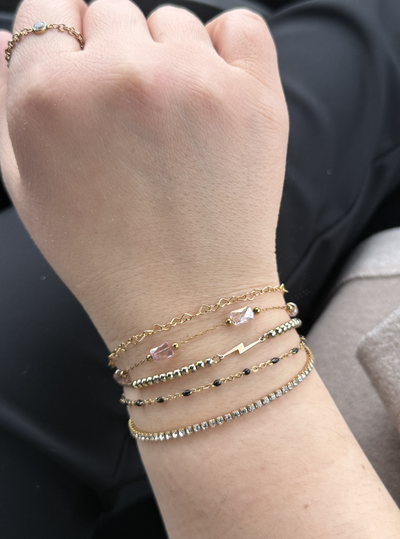 Stack of gold and beaded permanent bracelets on wrist with charm detail.