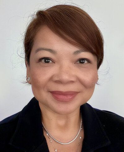 Headshot of Lorena Gatdula. She is a brunette, with swooped bangs, wearing a black blazer.