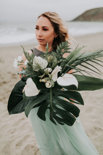 Bride holding a giant tropical bouquet and looking off to the distance