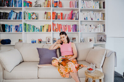 Perth Nutritionist sitting on couch reading in front of rainbow book shelf
