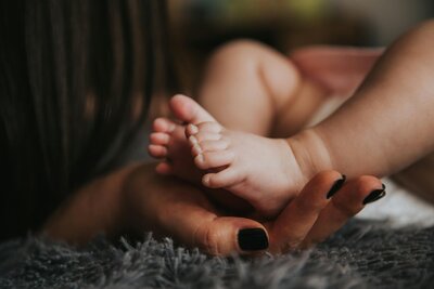 Woman's hands with black nail polish, holding tiny baby feet.