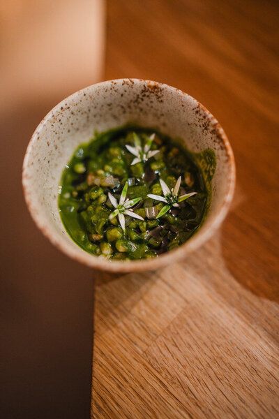 Rustic ceramic bowl filled with green herb sauce, lentils, and garnished with edible white flowers.