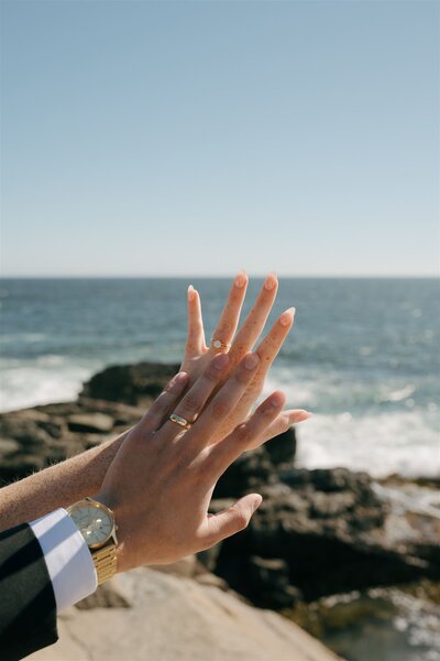 A bride and groom holding their hands up to the sky after their ceremony at Acadia National Park in Maine. 