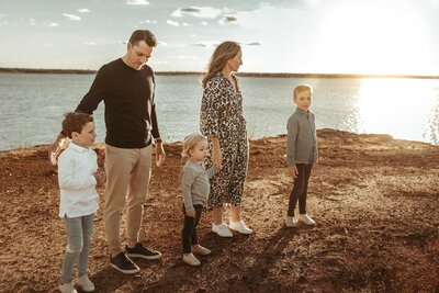 Big family holds hands by a lake. Dressed in black, gray and white matching outfits.The sky is blue and it is the perfect outdoor scene of a Texas golden hour.