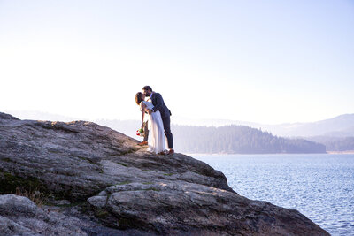 Bride and Groom on rock cliff bride dipped back letting arm drop holding bouquet.