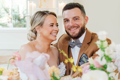 Capturing the joy of a newlywed couple as they share a laugh amidst a beautifully decorated wedding reception filled with elegant floral arrangements and warm, natural light.