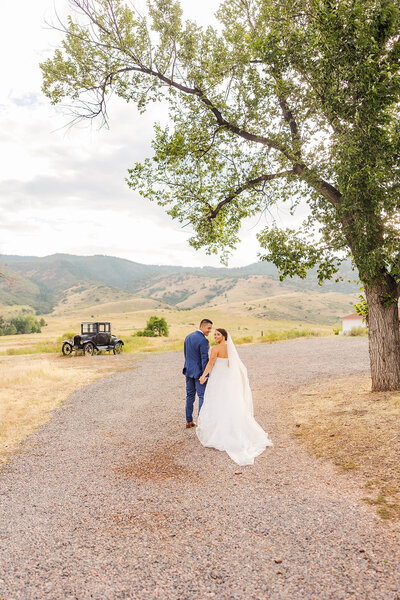 Bride and groom walking hand in hand on their wedding day at the Manor House in Littleton, Colorado, with a picturesque mountain backdrop enhancing their romantic journey.