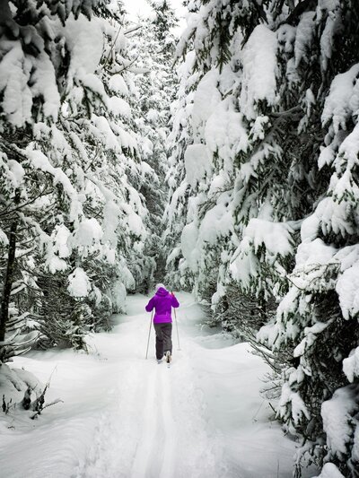 Woman skiing through the snowy road of Pincher Creek, surrounded with pine trees