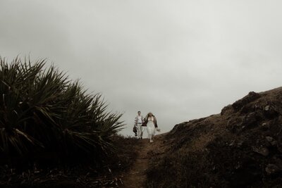 Yeppoon Elopement On a cliff over looking the ocean. Bride and Groom hiking with jackets on