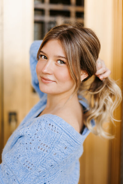 Close up portrait of a senior girl wearing a blue sweater and holding her hair back