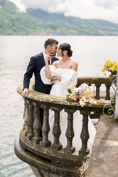 bride and groom embracing while standing on balcony over water